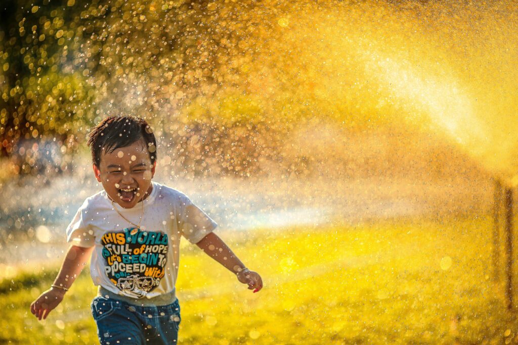 A child runs playfully through a sprinkler.