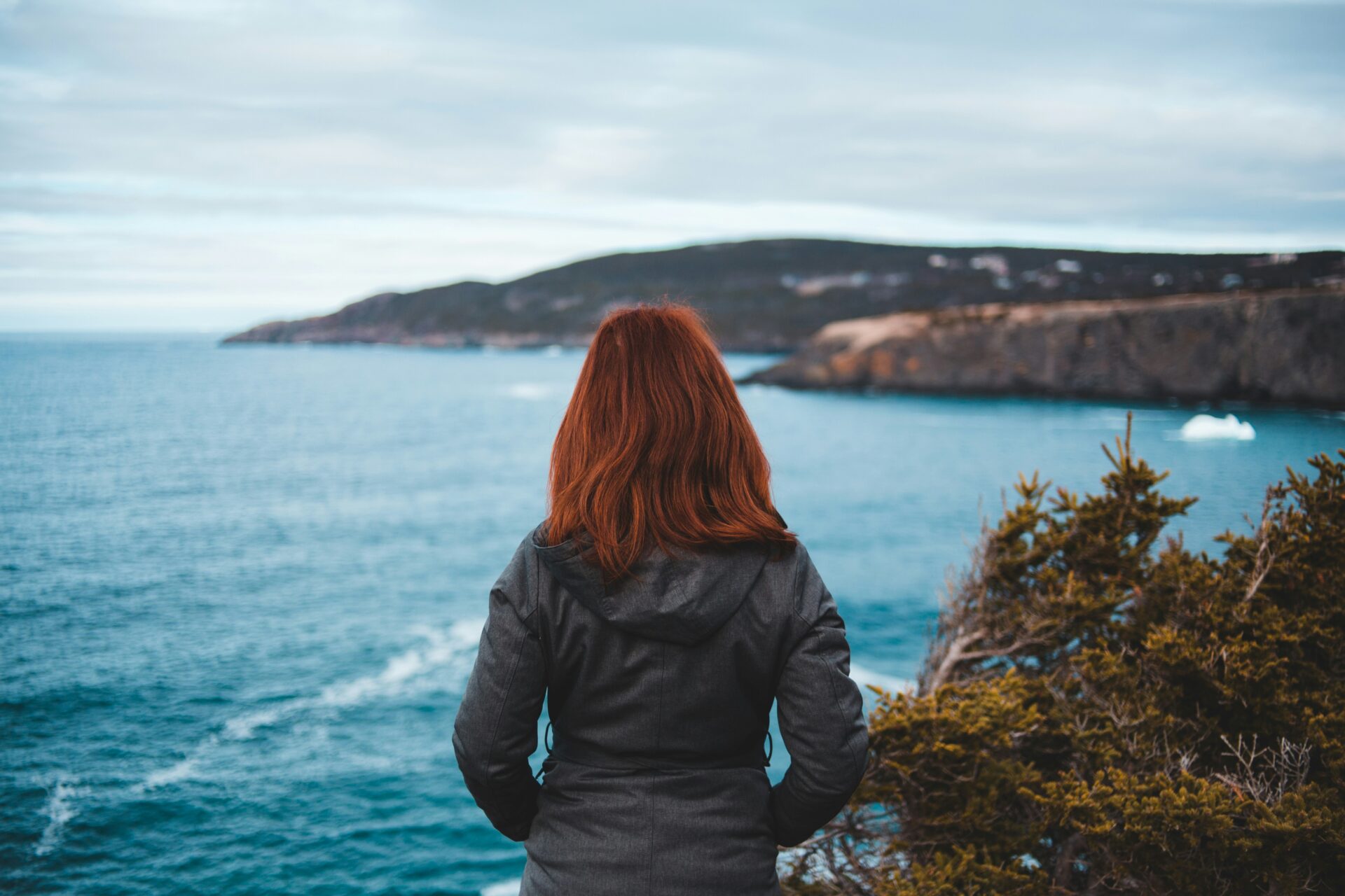 Woman faces away from camera, looking into ocean in the distance.