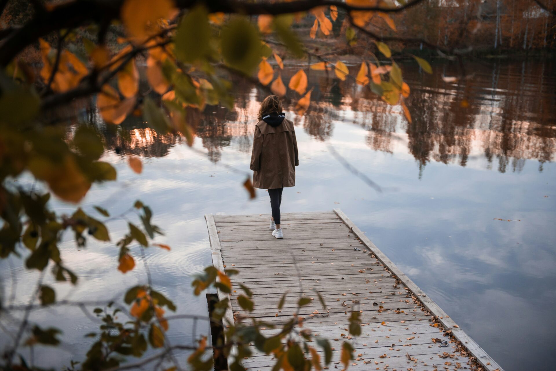 A woman stands on a dock alone looking over calm water.