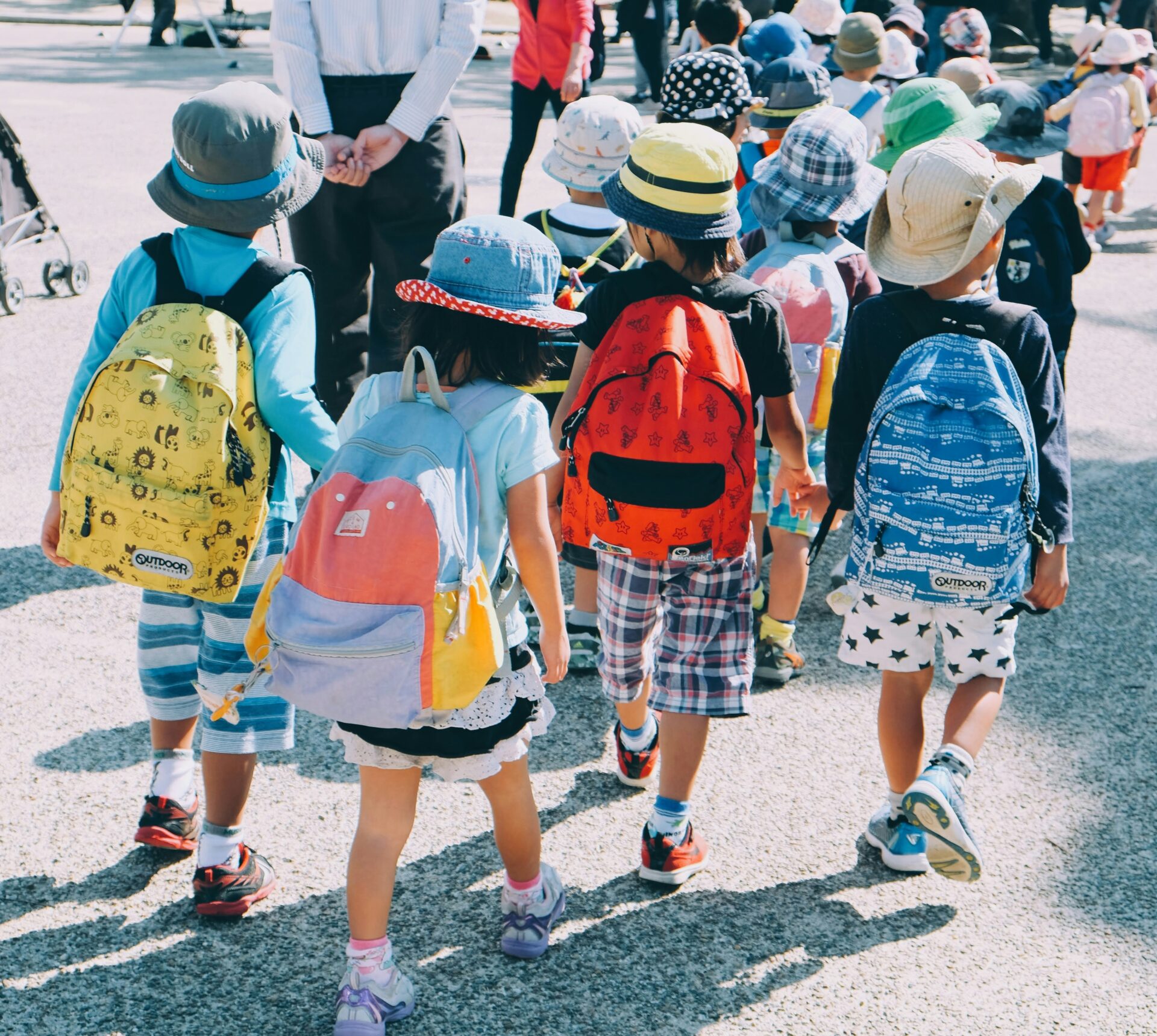 A group of young children wearing backpacks hold hands and walk to school together.