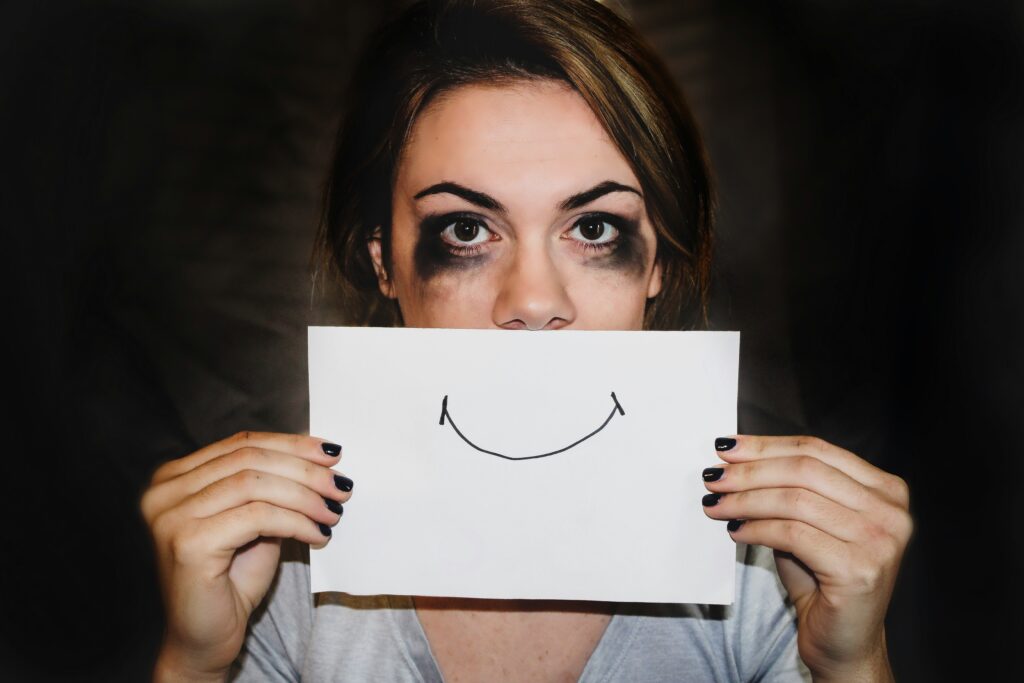 Sad woman hides behind sign of a smile.