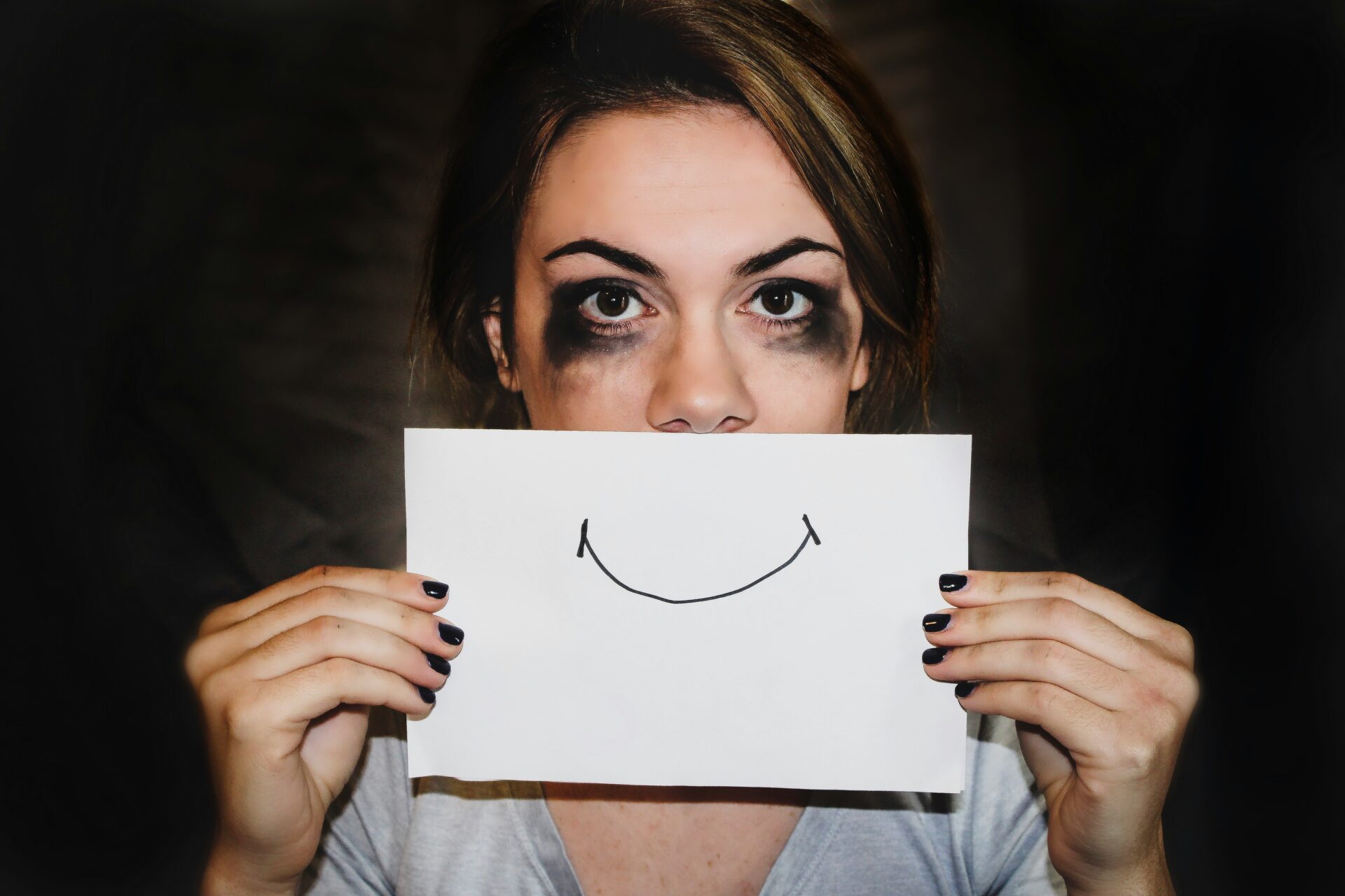 Sad woman hides behind sign of a smile.